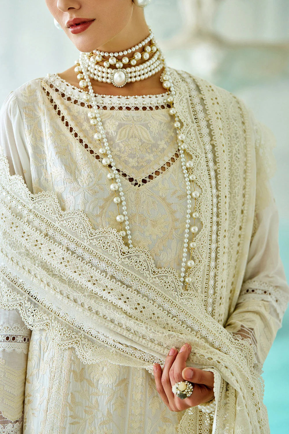 Person wearing a white embroidered dress with a matching shawl and pearl jewelry.