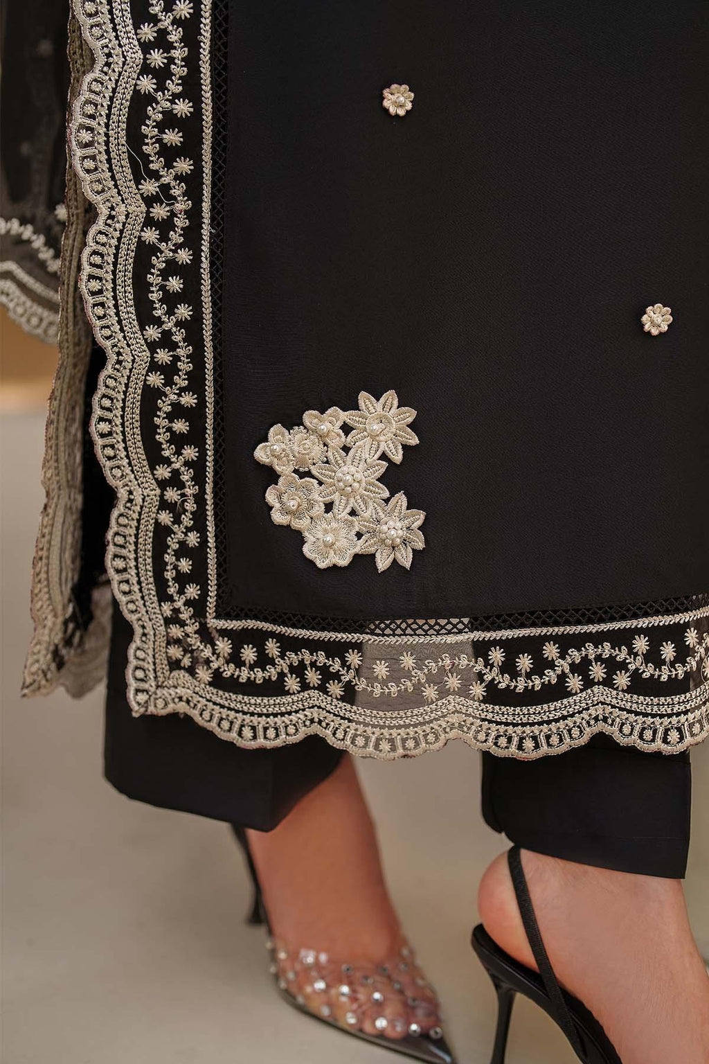 Black outfit with intricate white embroidery and embellishments on a neutral background
