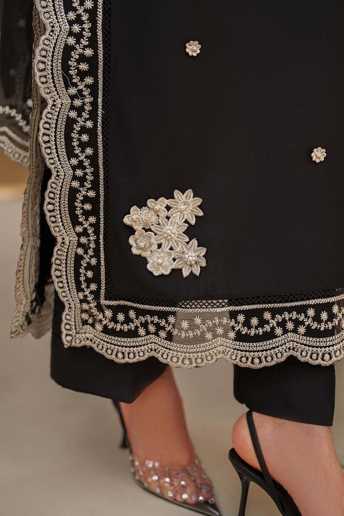 Black outfit with intricate white embroidery and embellishments on a neutral background