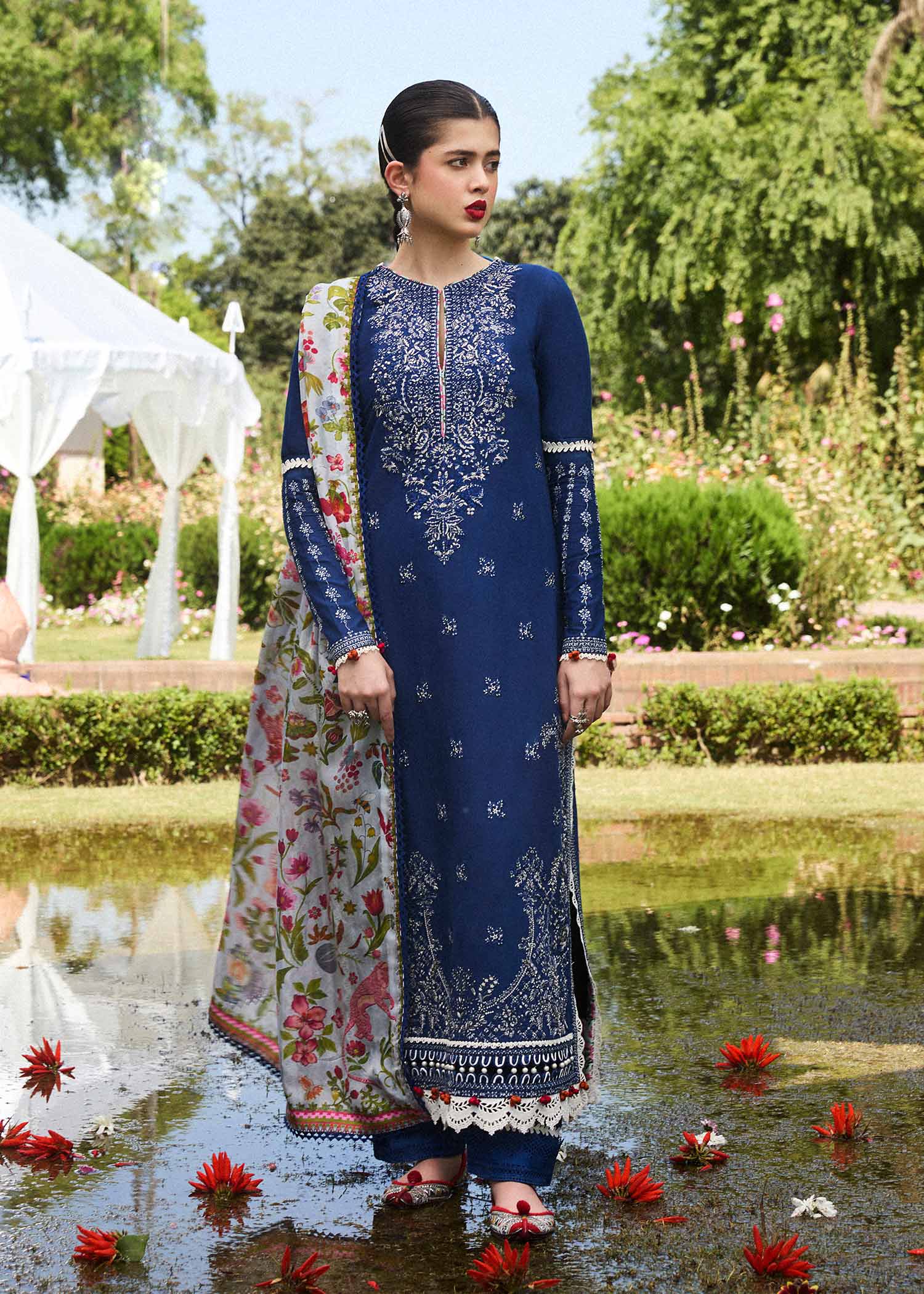 Woman in a blue embroidered dress standing by a pond with greenery in the background