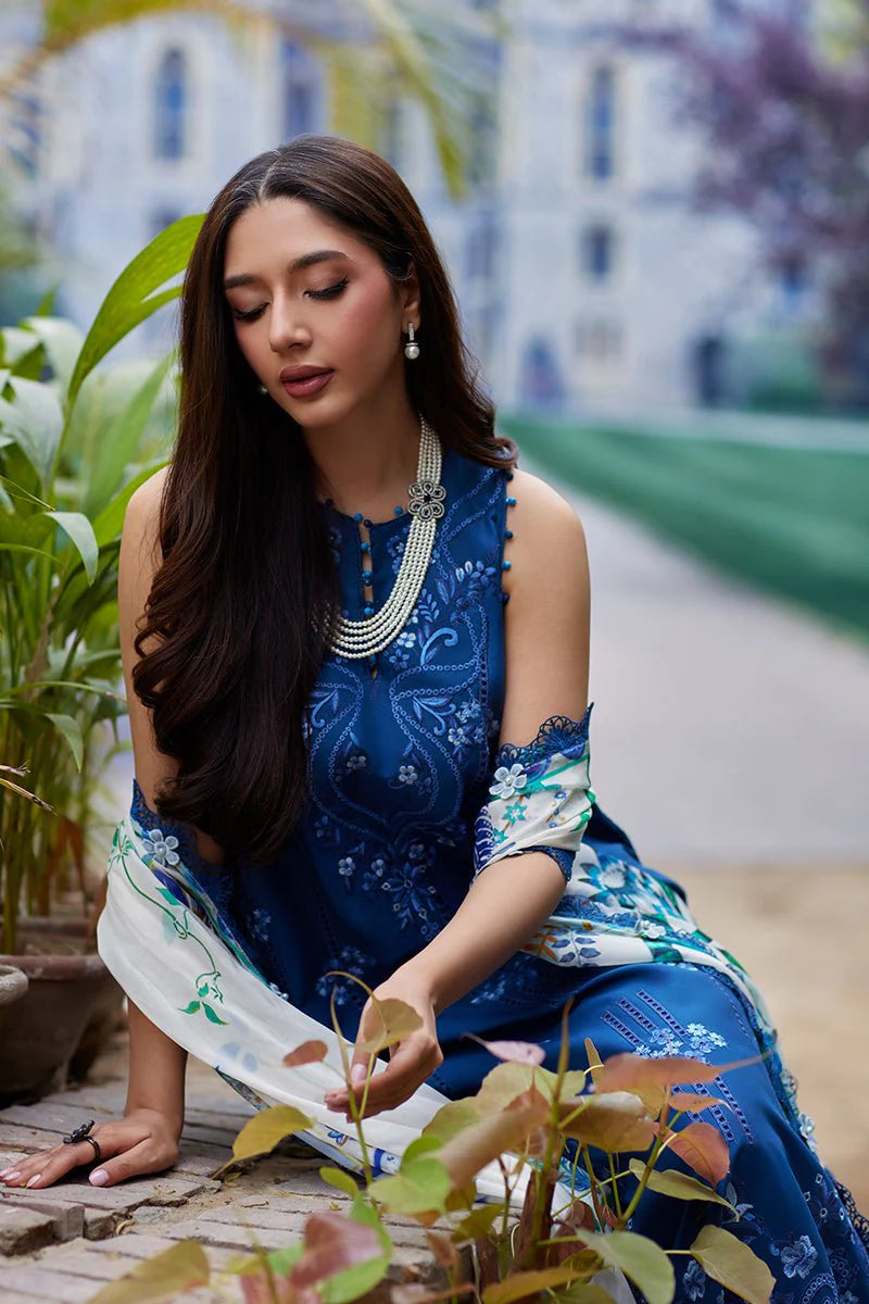 Woman in a blue and white traditional outfit sitting among plants with a blurred garden background