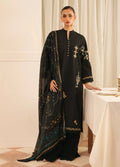 A woman models a black traditional outfit with gold and teal embroidery, featuring a long kurta, matching pants, and a sheer embroidered dupatta, set against a warm cream-colored indoor background.