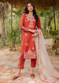A woman models a traditional three-piece salwar kameez suit in terracotta red with intricate white embroidery, paired with matching cropped trousers and a sheer beige dupatta, set against a tropical garden patio background.