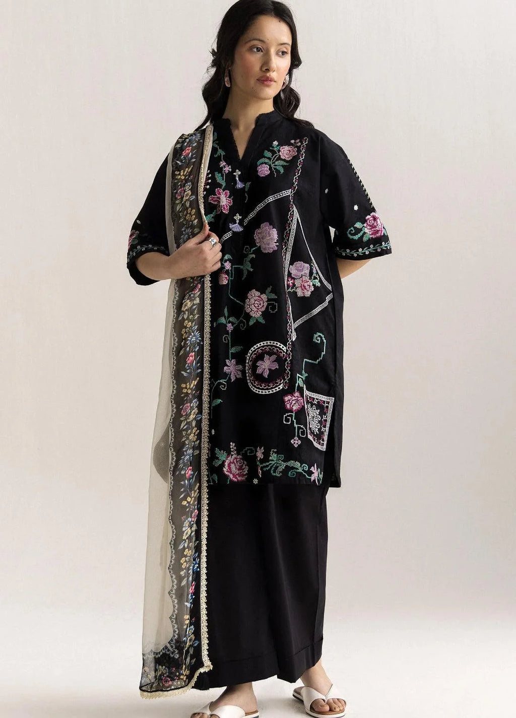 Woman wearing a black embroidered outfit with a long floral scarf on a white background
