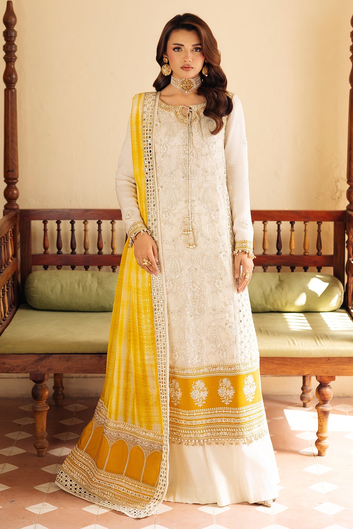 Woman wearing a white and yellow traditional outfit in a room with wooden furniture.