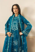 Woman wearing a teal embroidered outfit with a matching shawl against a beige background