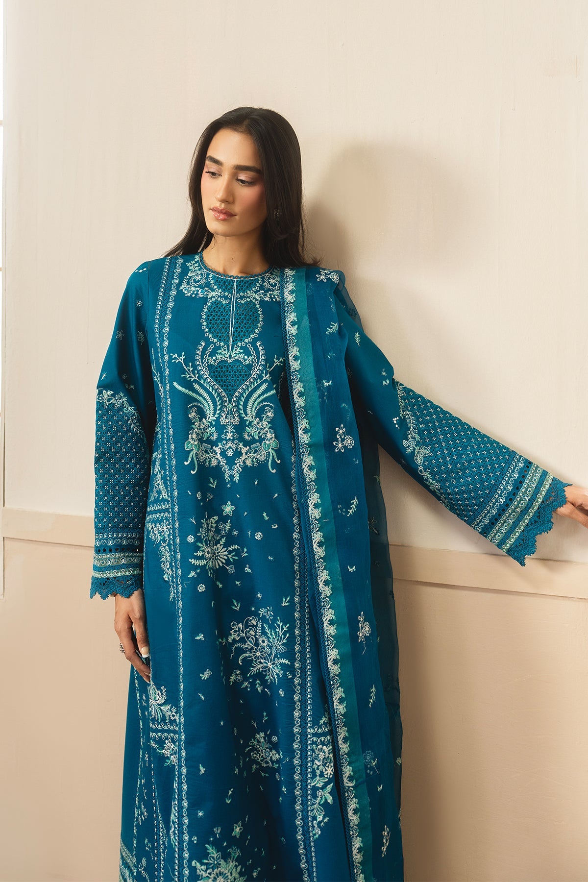 Woman wearing a teal embroidered dress against a beige wall
