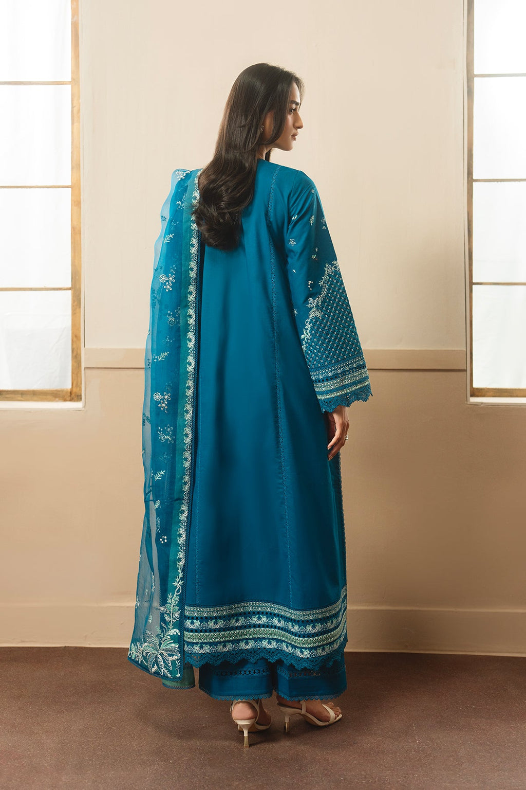 Woman wearing a blue traditional outfit with a matching dupatta in a room with beige walls and brown carpet.