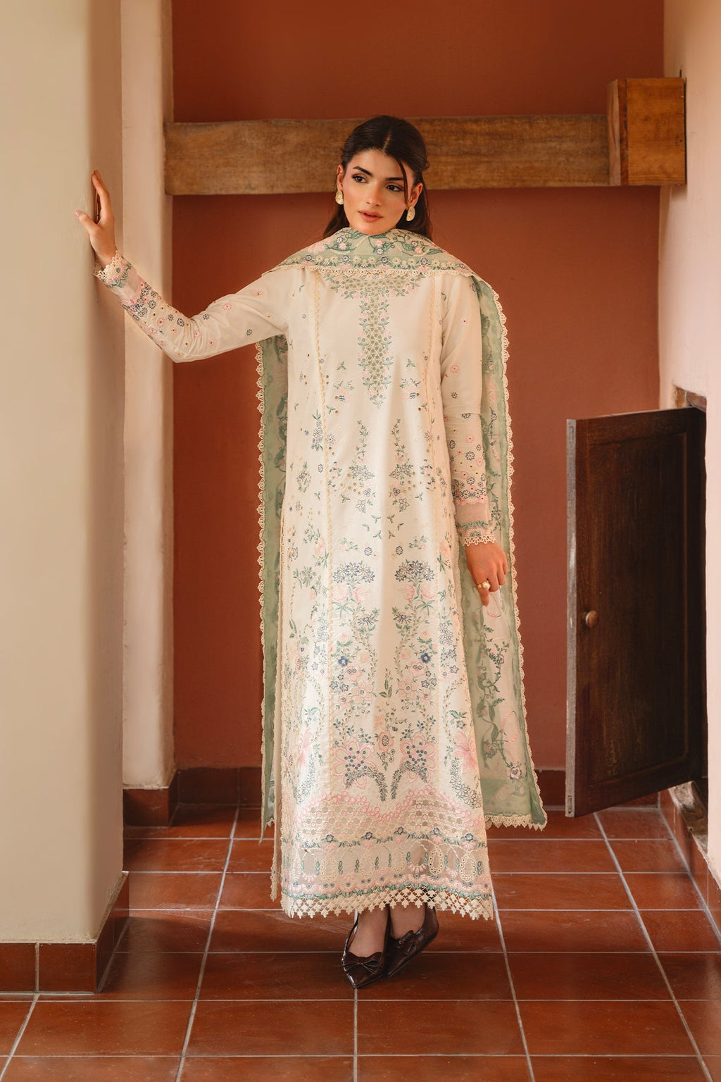 Woman wearing a traditional embroidered outfit in a room with tiled floor and wooden door.