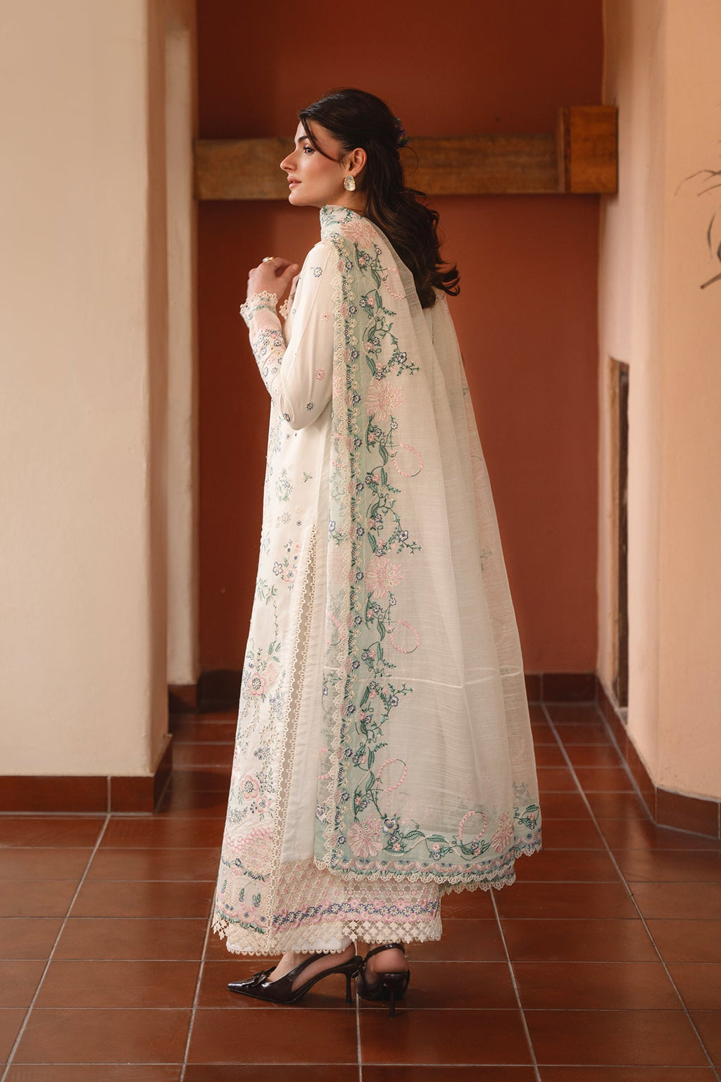 Woman in a white embroidered traditional outfit standing in a hallway.